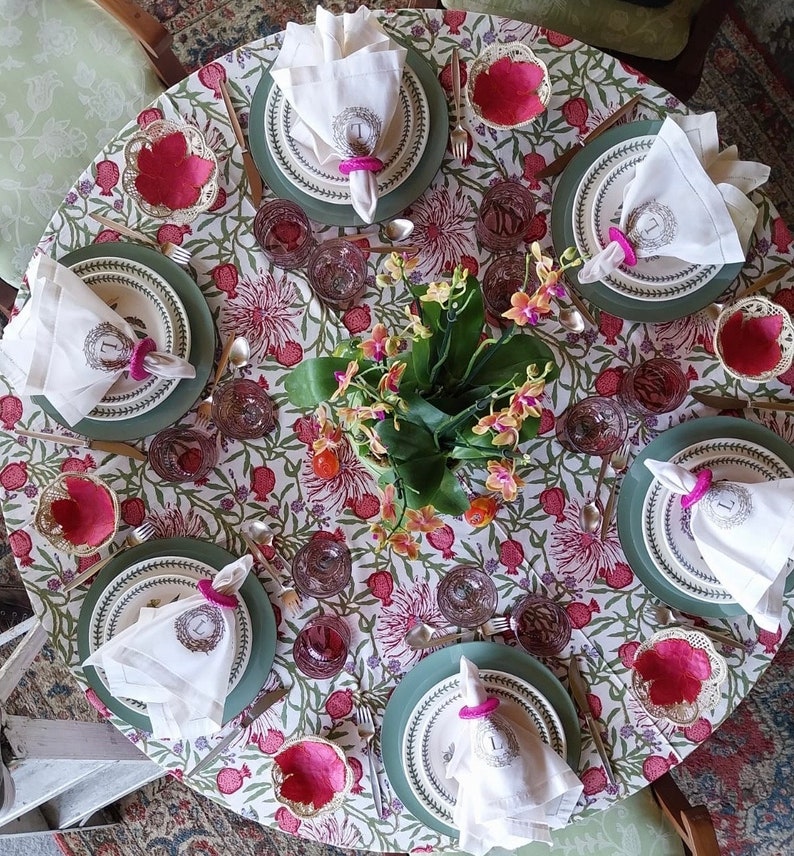 Puede incluir: Un mantel de mesa floral con un patr&oacute;n rosa y verde. Hay siete cubiertos con servilletas blancas, platos verdes y cuencos rosas. Las servilletas est&aacute;n dobladas y tienen un anillo con la letra 'L' en ellas.