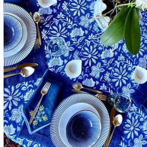 Peut inclure: Une table dress&eacute;e avec une nappe &agrave; motifs floraux bleus et blancs. L'ensemble comprend des assiettes &agrave; rayures blanches et bleues, de petits bols blancs, des couverts dor&eacute;s et des serviettes bleues. Des verres transparents sont &eacute;galement pr&eacute;sents.