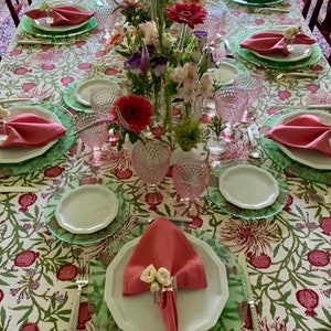 Puede incluir: Una mesa puesta con un mantel blanco con un patr&oacute;n floral. La mesa est&aacute; puesta con servilletas rosas, platos blancos y manteles individuales verdes. Tambi&eacute;n hay vasos rosas y un ramo de flores rosas y blancas en el centro de la mesa.