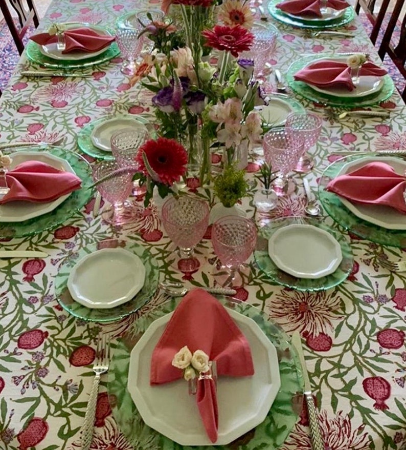 Puede incluir: Una mesa puesta con un mantel blanco con un patr&oacute;n floral. La mesa est&aacute; puesta con servilletas rosas, platos blancos y manteles individuales verdes. Tambi&eacute;n hay vasos rosas y un ramo de flores rosas y blancas en el centro de la mesa.