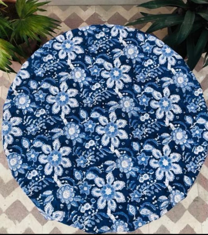 Peut inclure: Une nappe ronde avec un motif floral bleu et blanc. Le motif pr&eacute;sente de grandes fleurs stylis&eacute;es et de plus petits &eacute;l&eacute;ments floraux dans diff&eacute;rentes nuances de bleu sur un fond bleu fonc&eacute;. La nappe est en tissu doux.