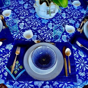 Peut inclure: Une table joliment dress&eacute;e avec des assiettes, des bols et une nappe &agrave; motifs bleus et blancs. Des couverts dor&eacute;s et de petits bols blancs ajoutent de l'&eacute;l&eacute;gance. La table comprend des verres et un vase d&eacute;coratif, cr&eacute;ant une exp&eacute;rience culinaire harmonieuse.