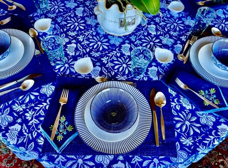 Peut inclure: Une table joliment dress&eacute;e avec des assiettes, des bols et une nappe &agrave; motifs bleus et blancs. Des couverts dor&eacute;s et de petits bols blancs ajoutent de l'&eacute;l&eacute;gance. La table comprend des verres et un vase d&eacute;coratif, cr&eacute;ant une exp&eacute;rience culinaire harmonieuse.