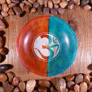 May include: A round wooden bowl with a teal and orange finish. The bowl has a carved Om symbol in the center.