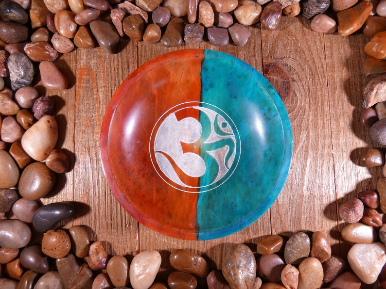 May include: A round wooden bowl with a teal and orange finish. The bowl has a carved Om symbol in the center.