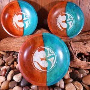 May include: Three wooden bowls with a teal and brown finish. Each bowl features a white Om symbol carved into the center.