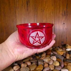 May include: A red stone bowl with a white pentagram carved into the bottom. The bowl is being held in a hand.