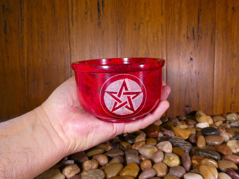 May include: A red stone bowl with a white pentagram carved into the bottom. The bowl is being held in a hand.