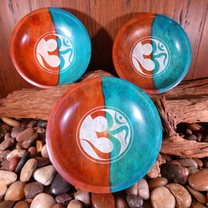 May include: Three wooden bowls with a teal and reddish-brown finish. Each bowl features a white Om symbol carved into the surface.