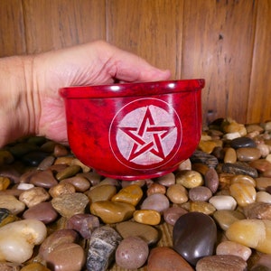 May include: A red stone bowl with a white pentagram carved into the centre. The bowl is being held by a hand.