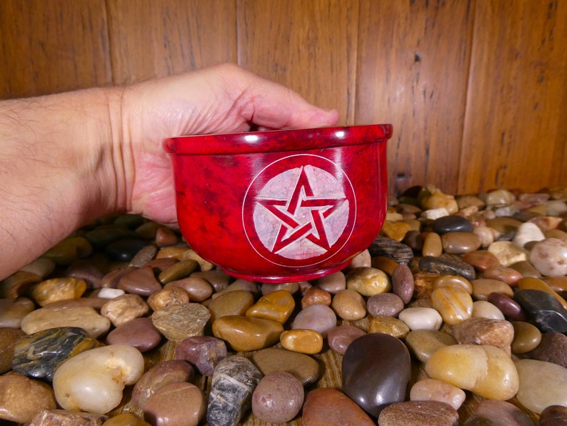 May include: A red stone bowl with a white pentagram carved into the centre. The bowl is being held by a hand.