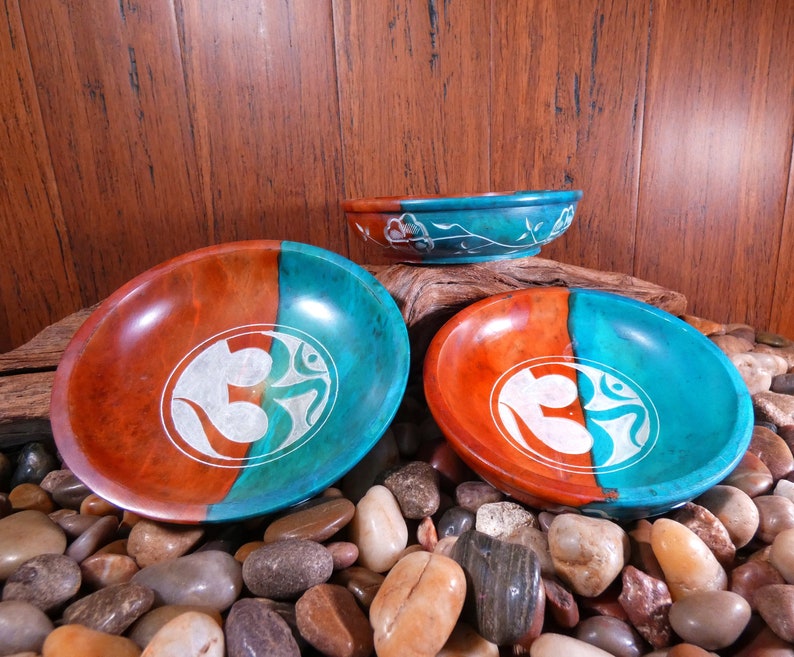 May include: Three round, wooden bowls with a teal and orange glaze. Each bowl features a white Om symbol carved into the surface.