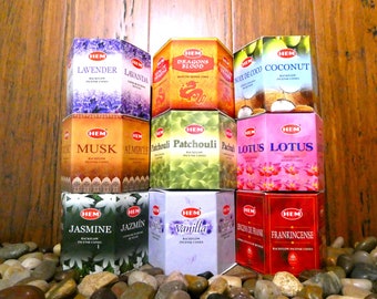 May include: A collection of ten hexagonal boxes of HEM brand backflow incense cones. The boxes are arranged in a pyramid shape and feature a variety of scents, including Lavender, Dragons Blood, Coconut, Musk, Patchouli, Lotus, Jasmine, Vanilla, and Frankincense.
