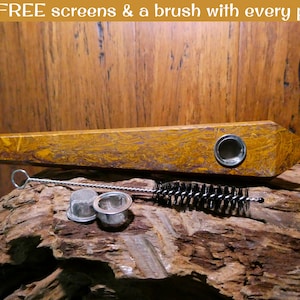 May include: A wooden pipe with a brown and gold marbled finish. The pipe is on a wooden surface with a metal pipe cleaner, two metal screens, and a black brush.