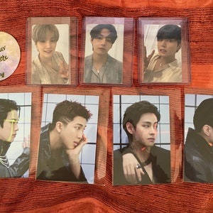 May include: Seven photo cards featuring different members of a K-pop group. The cards are all in a similar style, with a white background and a grid pattern. The members are all wearing different outfits, and some are looking directly at the camera while others are looking off to the side.