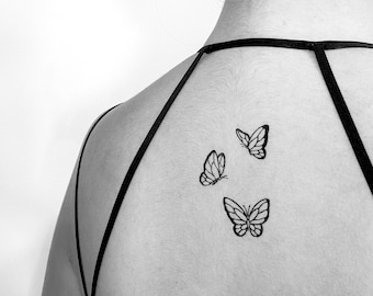 May include: A black and white photo of a person's back with three small butterfly tattoos.
