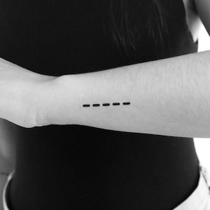 Op de afbeelding: Een zwart-witfoto van een arm met een eenvoudige tatoeage van vijf streepjes op de pols.