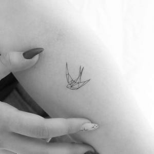 May include: A geometric line drawing of a swallow tattoo on a person's arm.
