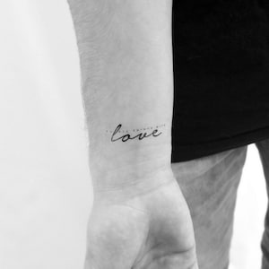 Peut inclure: Une photo en noir et blanc d'un poignet avec un tatouage qui dit "Do all things with love."