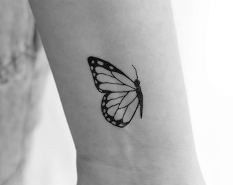 May include: A black and white outline of a butterfly tattoo on a person's wrist.