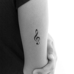 Op de afbeelding: Een zwart-witte tijdelijke tattoo van een vioolsleutel op de arm van een persoon.