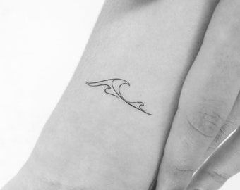 May include: A minimalist black line art tattoo of a stylized wave design. The wave is depicted with flowing lines, creating a sense of movement and fluidity. The tattoo is on the wrist.