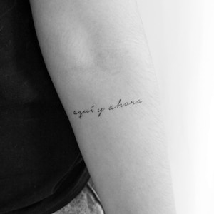 Könnte beinhalten: Ein Schwarzweißfoto eines Arms mit einem Tattoo, auf dem in Kursivschrift "aquí y ahora" steht.