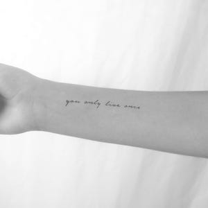Peut inclure: Une photo en noir et blanc d'un bras avec un tatouage qui dit "you only live once".