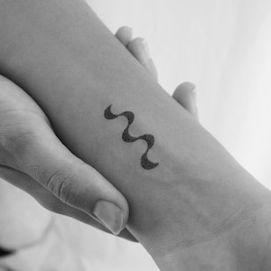 May include: A black and white tattoo of a wavy line on a person's arm.