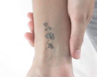 Può includere: Un piccolo tatuaggio floreale delicato sul polso di una persona. Il tatuaggio presenta un unico stelo con tre piccoli fiori rotondi.