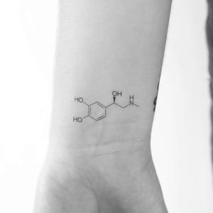 Könnte beinhalten: Eine schwarz-weiße Linienzeichnung einer chemischen Formel für Dopamin, einen Neurotransmitter, die auf das Handgelenk einer Person tätowiert ist.