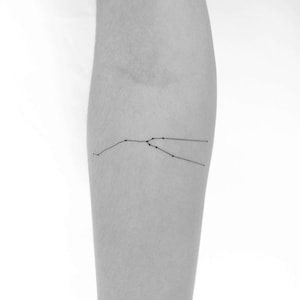 Op de afbeelding: Een zwart-wit afbeelding van een sterrenbeeld tatoeage op de arm van een persoon. Het sterrenbeeld is Stier.