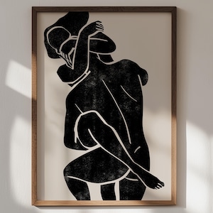 Puede incluir: Lámina de arte abstracto que presenta una ilustración en blanco y negro de dos figuras abrazándose. La obra de arte está enmarcada en un marco de madera natural y colocada sobre un fondo neutro. Las figuras están representadas con líneas audaces y un aspecto texturizado.