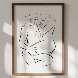 May include: A framed wall art print featuring a black line drawing of two figures in an intimate embrace. The artwork is presented on a white background within a dark brown wooden frame, showcasing a minimalist contour style of two human bodies.
