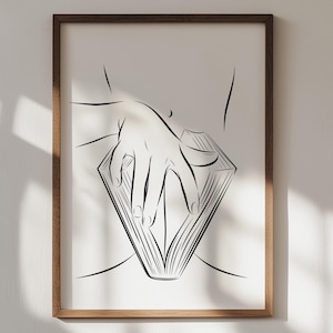 May include: A framed art print featuring a minimalist line drawing. The artwork depicts a hand resting on an open book, with the book's pages forming a diamond shape. The drawing is in black against a white background, encased in a brown wooden frame.