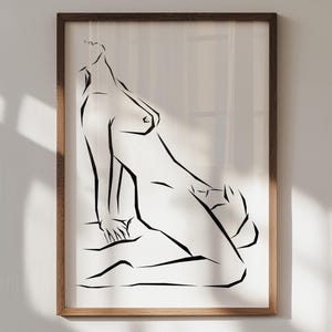 May include: A framed art print featuring a minimalist line drawing of a reclining figure. The artwork is rendered in black lines on a white background, encased in a brown wooden frame. The figure is depicted in a sensual pose.