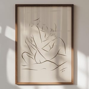 Puede incluir: Una impresión artística enmarcada con un dibujo lineal minimalista de dos figuras abrazándose. La obra de arte está realizada en líneas negras sobre un fondo crema, dentro de un marco de madera natural. La pieza evoca intimidad y conexión.