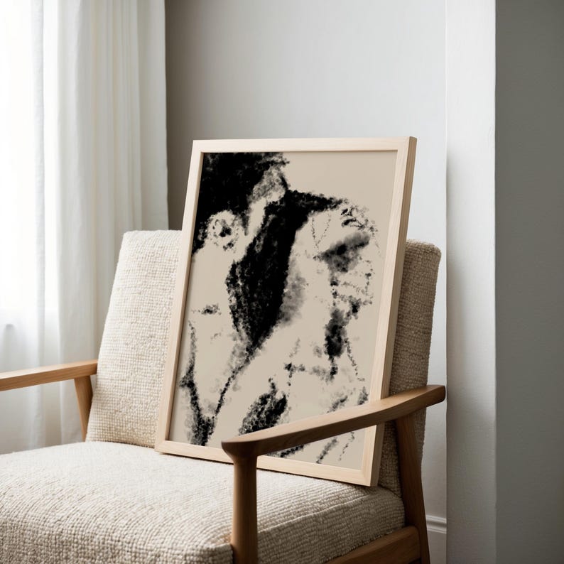 Puede incluir: Una impresi&oacute;n art&iacute;stica abstracta en blanco y negro enmarcada. La obra presenta un boceto a carboncillo de dos figuras. El marco es de madera clara y la impresi&oacute;n se muestra en una silla beige con brazos de madera.