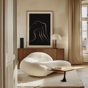 May include: A white, modern, curved sofa with a white, fluffy rug underneath. A black and white line art print hangs above a wooden cabinet. A small, round, black and white table sits in front of the sofa.