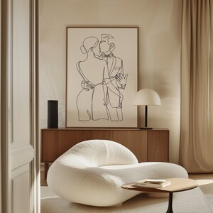 K&ouml;nnte beinhalten: Eine Schwarz-Wei&szlig;-Zeichnung eines sich k&uuml;ssenden Paares, gerahmt und an einer Wand &uuml;ber einem wei&szlig;en Sofa und einem Holztisch h&auml;ngend.