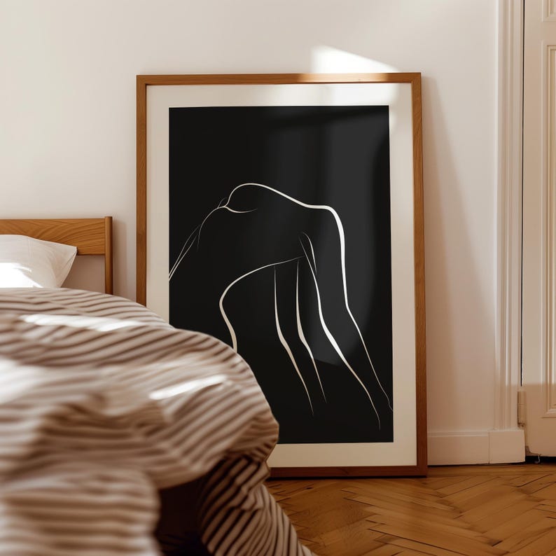 May include: A black and white line art print of a person's body in a relaxed pose. The print is framed in a natural wood frame.