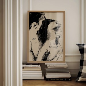 Puede incluir: Una impresi&oacute;n art&iacute;stica enmarcada con un boceto en blanco y negro de dos figuras. La obra de arte tiene un fondo neutro y est&aacute; enmarcada en un marco de madera marr&oacute;n claro. La impresi&oacute;n descansa sobre una pila de libros.