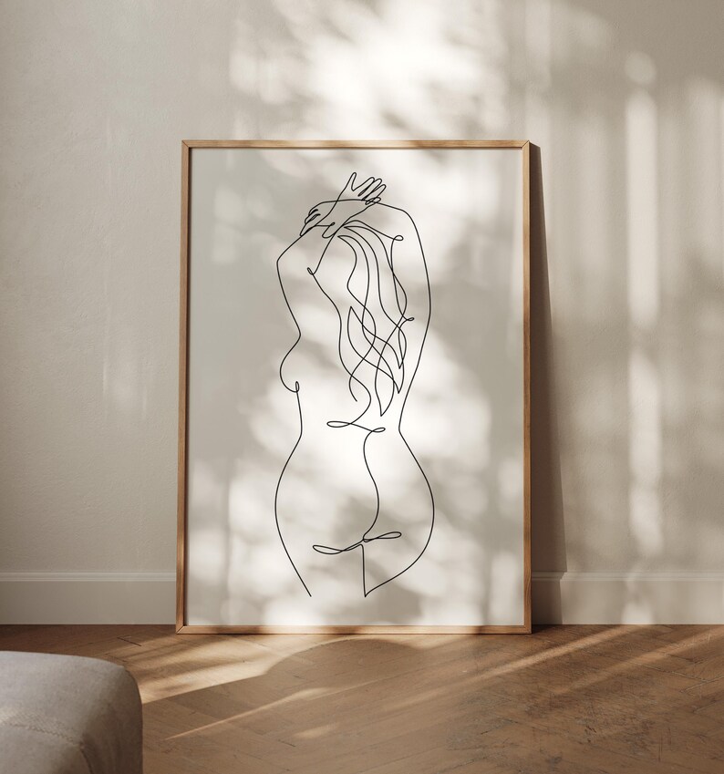 Puede incluir: Una impresi&oacute;n art&iacute;stica enmarcada con un dibujo lineal minimalista de la espalda de una persona. El arte lineal negro representa la forma de la figura, con los brazos levantados hacia la cabeza y el pelo suelto. La obra de arte est&aacute; sobre un fondo neutro.
