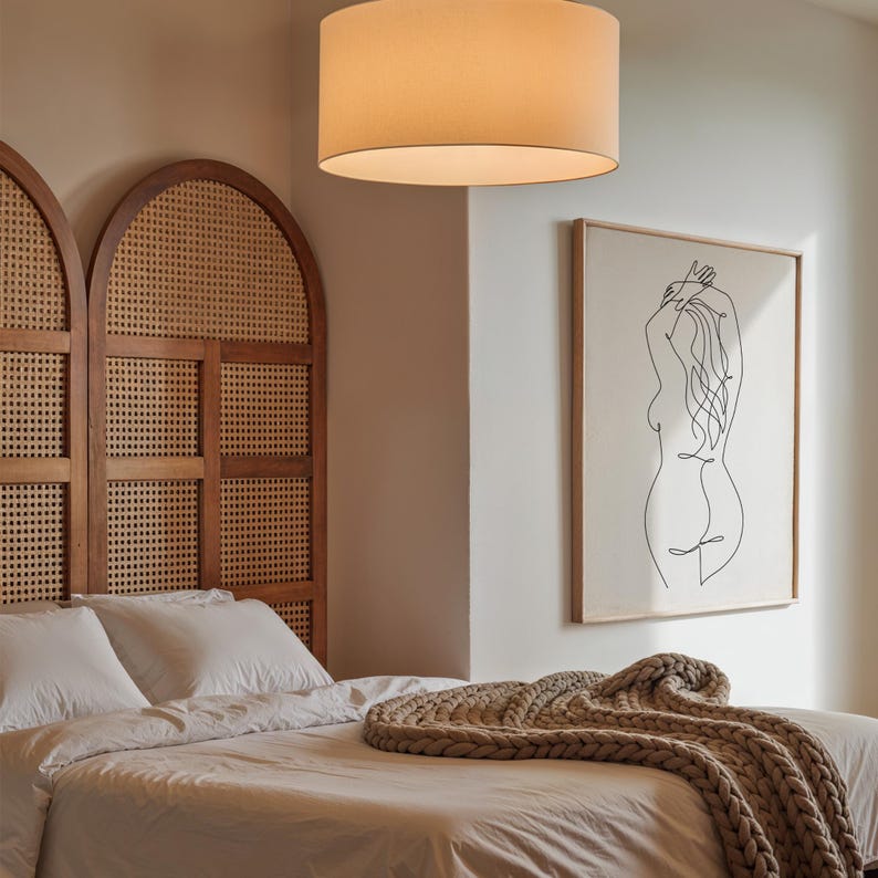 Puede incluir: Una habitaci&oacute;n con una cama con s&aacute;banas blancas, un cabecero tejido y una gran impresi&oacute;n de arte lineal enmarcada. Una manta de punto grueso beige descansa sobre la cama. Una l&aacute;mpara colgante beige con forma de tambor cuelga del techo.