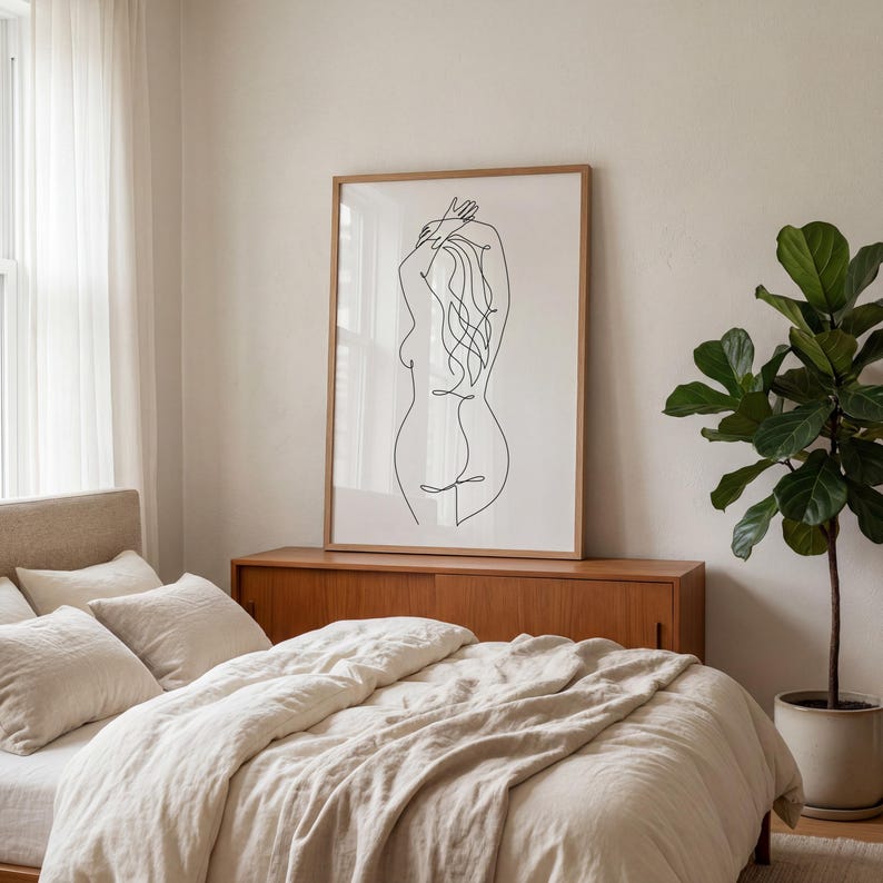 Puede incluir: Una impresi&oacute;n art&iacute;stica enmarcada con un dibujo lineal minimalista de una figura humana. La obra de arte negra se encuentra sobre un fondo blanco, dentro de un marco de madera. La impresi&oacute;n se muestra sobre un mueble de madera en un dormitorio, con una cama y una planta en maceta.