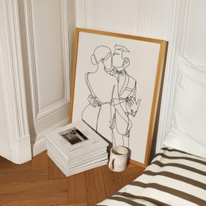 K&ouml;nnte beinhalten: Eine Schwarzwei&szlig;-Linienzeichnung eines sich k&uuml;ssenden Paares. Die Zeichnung ist in einem goldenen Rahmen gerahmt und h&auml;ngt an einer wei&szlig;en Wand. Das Paar ist in festlicher Kleidung gekleidet.