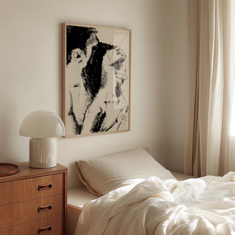 Puede incluir: Una escena de dormitorio con una impresi&oacute;n art&iacute;stica abstracta enmarcada en tonos negros y beige. Una l&aacute;mpara blanca con forma de hongo est&aacute; sobre una c&oacute;moda de madera. La cama est&aacute; hecha con s&aacute;banas blancas y una cortina beige a la derecha.