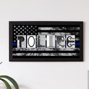 Peut inclure: Tableau encadré avec le mot "POLICE" épelé en lettres individuelles sur un fond de drapeau américain noir et blanc. Une ligne bleue traverse le drapeau. L'œuvre est accrochée sur un mur blanc.