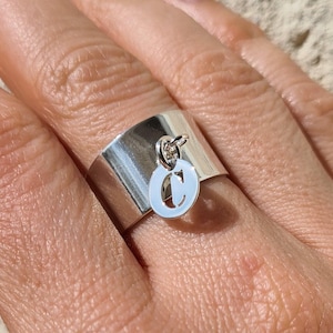 Peut inclure: Une bague en argent avec une large bande et un charme en forme de lettre "C".