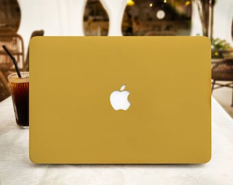 May include: A gold laptop with a white Apple logo on the lid. The laptop is sitting on a white surface.